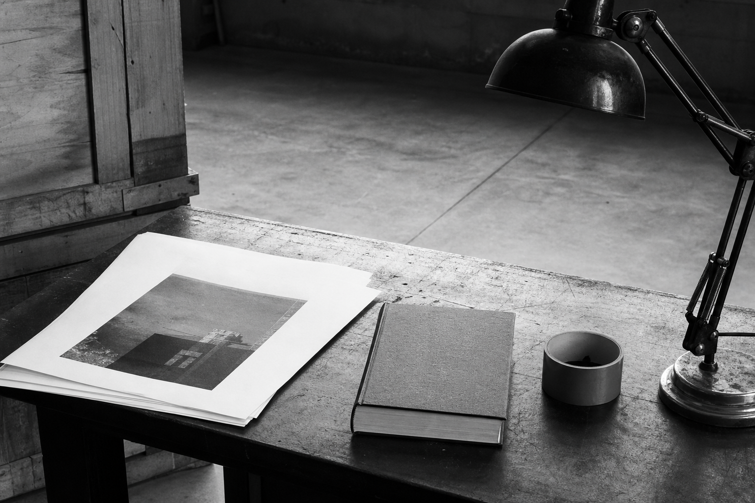 Black-and-white photo placeholder of an empty factory workbench with paper, a book, and a lamp. No people. Swap later for a real photo of the same motive.
